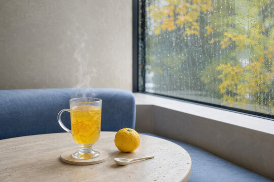 Taza de t&eacute; caliente junto a una ventana con gotas de lluvia y un lim&oacute;n en la mesa