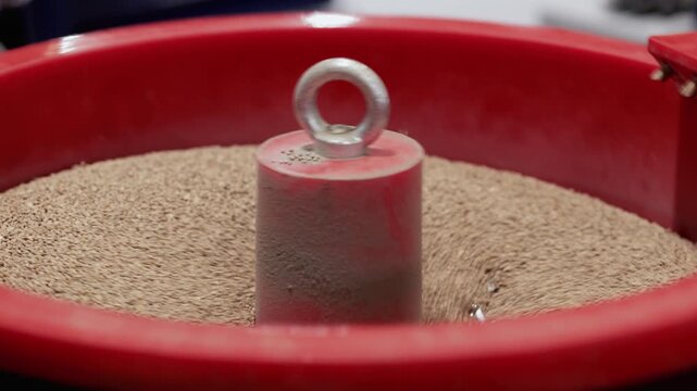 Polishing metal piece with vibrating drum full of ceramic particles in workshop closeup. High frequency friction removes scratches from surface at exhibition