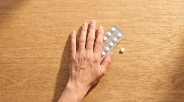Elderly hand reaching for pill blister pack on wooden table  