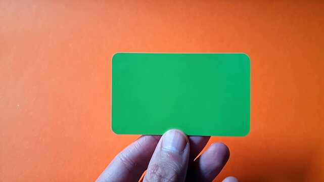 Hand holding a green card against a vibrant orange background, showcasing the card's color and texture in a clear, focused manner for visual emphasis and clarity