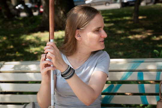 Blond haired visually impaired woman with white cane sitting in a public park