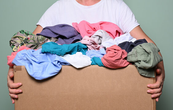 Female hands holding cardboard box with various clothes