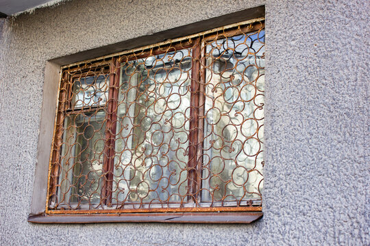Window grille. An old, dilapidated window with a rusty metal grille. An iron window.