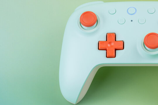 Close up of a mint green wireless game controller with orange buttons on a green gradient background with copy space