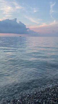 pastel evening light reflects over a calm sea beside a pebble shore, while distant ships and soft blue clouds create a serene coastal twilight background with gentle waves