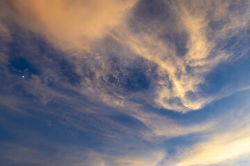 Obraz premium Golden cirrus cloud at sunset with soft blue sky and gentle warm light, serene atmospheric scene conveying calm and peaceful mood