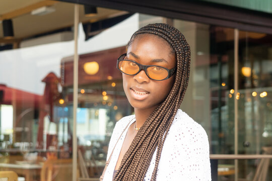 Young woman with an Afro braided hairstyle, orange glasses, and a white blouse