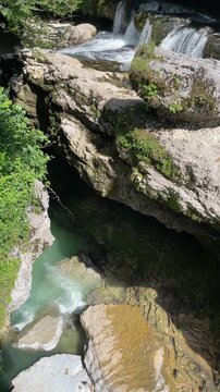 clear turquoise river rushes beneath layered limestone shelves in a shaded forest gorge, revealing mossy rocks, textured cliffs and a hidden freshwater canyon landscape