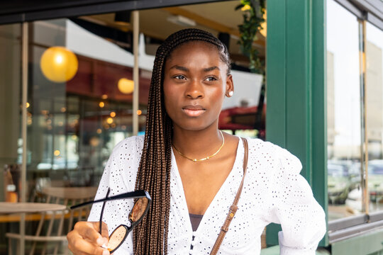 Young female model with an Afro braided hairstyle, holding orange glasses in her hand
