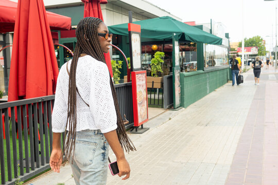 A teenage girl with an Afro braided hairstyle and orange glasses, walking away