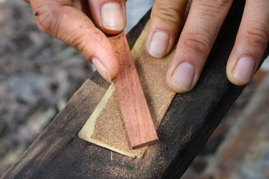Hand sanding small wooden strip on rough beam, close up of hands and woodwork showing texture and focus on craftsmanship and detail