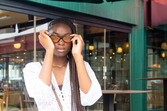 A young model with an Afro-braid hairstyle putting on orange glasses