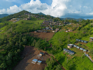 Fototapeta premium Hillside village with terraced houses and green vegetation under dramatic clouds, peaceful rural landscape with winding paths and scattered cabins conveying serenity and openness