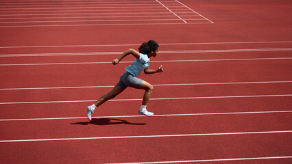Fototapeta premium Teenage female runner sprinting at full speed across red athletics track. Concept of speed development, track and field sports, summer competition.