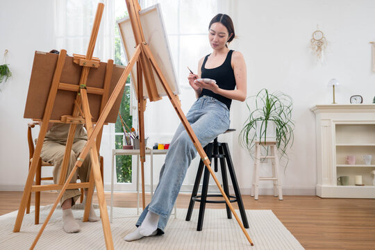 Two young Asian women painting a colorful landscape on canvas together