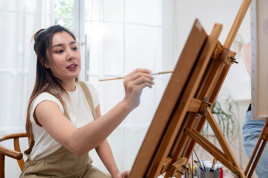 Young Asian woman painting on canvas in a bright home art studio during the weekend