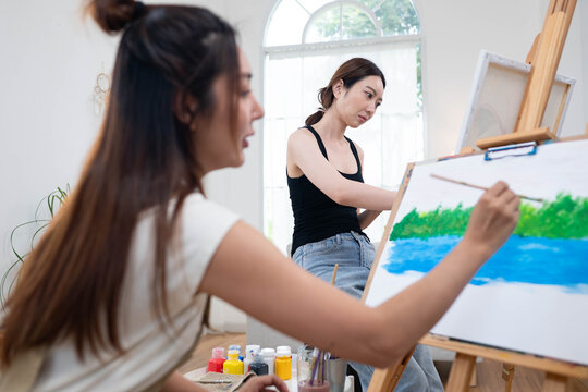 Two young Asian women painting a colorful landscape on canvas together