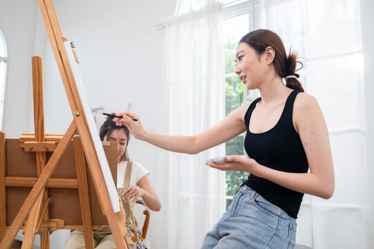 Two young Asian women painting a colorful landscape on canvas together