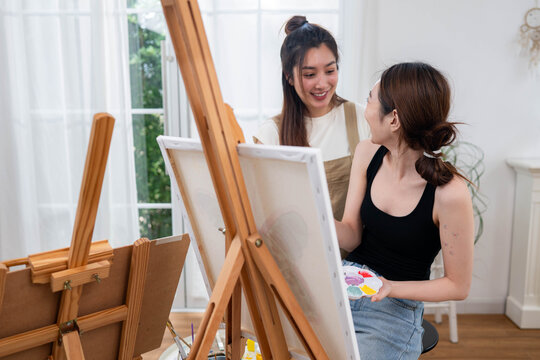 Two young Asian women painting a colorful landscape on canvas together