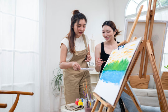 Two young Asian women painting a colorful landscape on canvas together