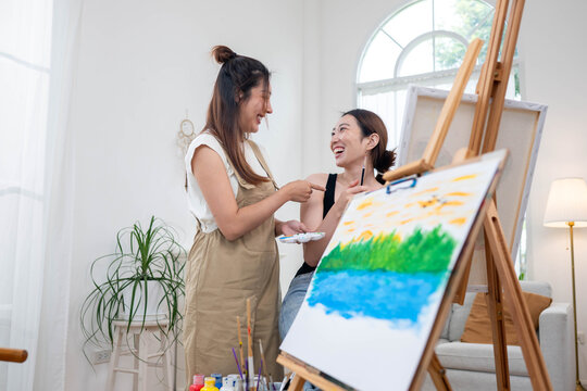 Two young Asian women painting a colorful landscape on canvas together