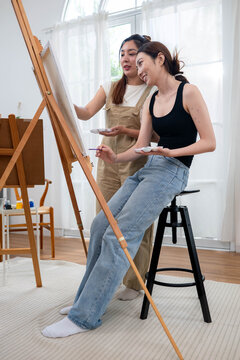 Two young Asian women painting a colorful landscape on canvas together
