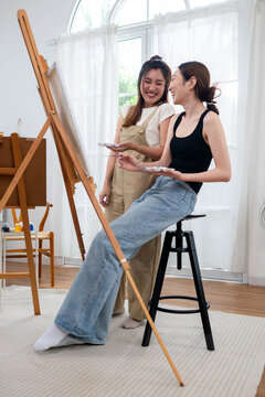 Two young Asian women painting a colorful landscape on canvas together