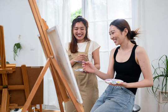 Two young Asian women painting a colorful landscape on canvas together