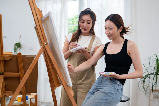 Two young Asian women painting a colorful landscape on canvas together