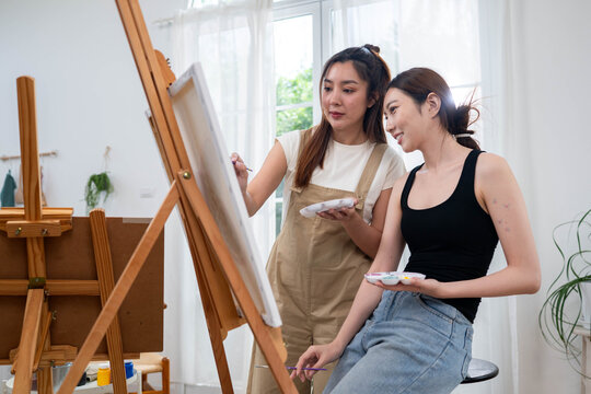 Two young Asian women painting a colorful landscape on canvas together
