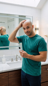 Caucasian man applying lotion to his bald head in the bathroom. Daily skincare and self-care routine for men. Personal hygiene and beauty product concept.