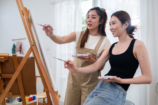 Two young Asian women painting a colorful landscape on canvas together