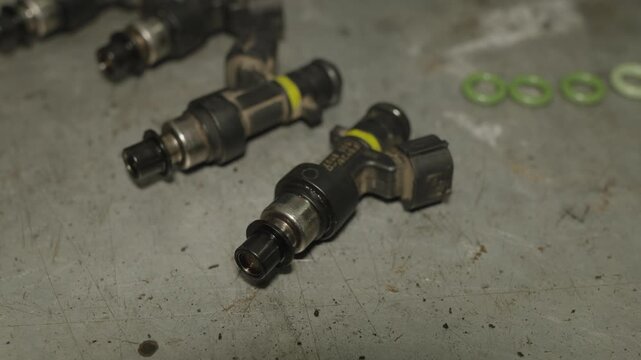 Four car fuel injectors lying on a scratched metallic workbench surface.