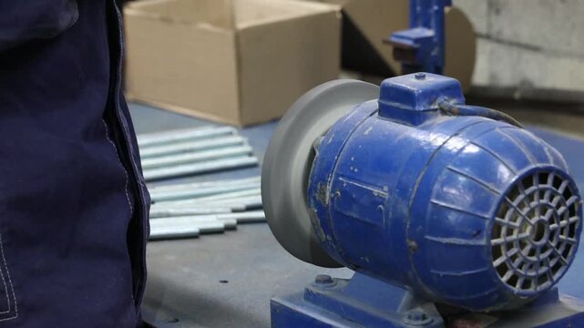 a worker is sharpening a threaded metal rod on a grinder