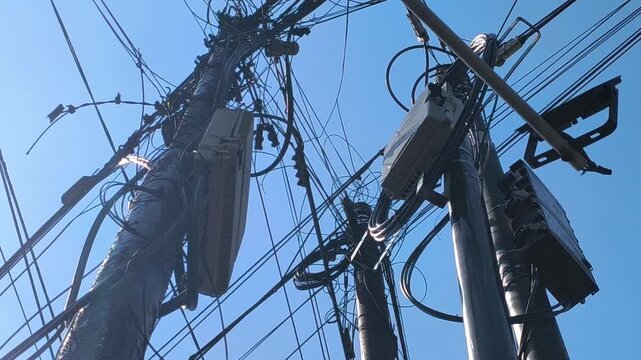 A utility pole supporting overhead power lines and tangled communication cables in an urban setting, illustrating electrical infrastructure, telecommunications networks, and city utility systems.