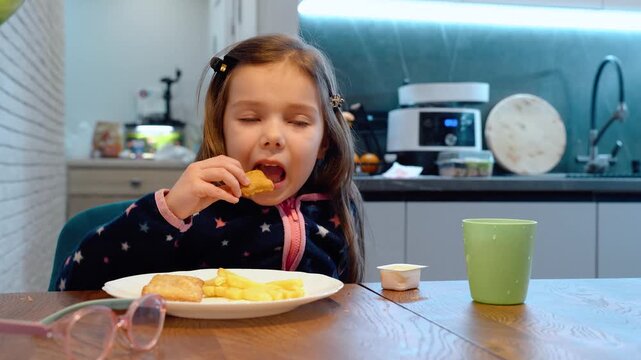 Young girl eating pastry beside fries at kitchen table with green mug, wooden countertop, soft home light, casual indoor meal scene with shallow focus and cozy everyday feel