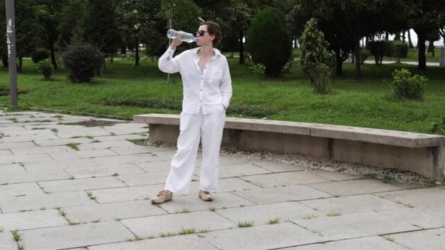 cancer survivor holding a water bottle pauses beneath open sky in a city park, combining hydration, fresh air and mindful recovery after treatment