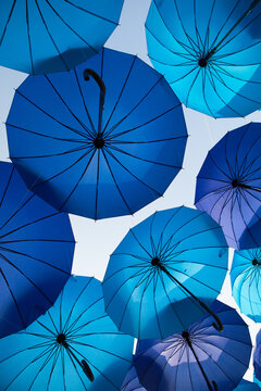 Blue umbrellas of varied sizes hang against the sky, colorful outdoor installation, creative decorative pattern, summer festival theme.