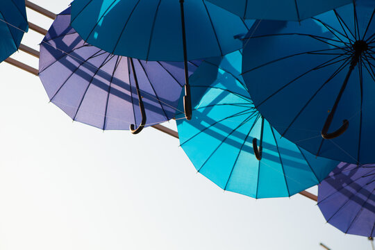 Blue and turquoise umbrellas hang along the edge of a bright open sky, minimalist outdoor decoration, creative travel background.