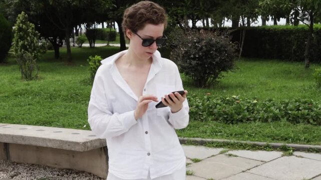 cancer survivor uses a phone while walking outdoors, illustrating remote communication with a care team, digital wellbeing and active recovery after oncology treatment in everyday life