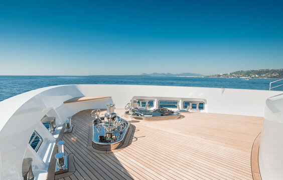 Bow of a new and modern Superyacht with teak deck, stainless steel capstans and cleats, with a nice view over blue sky and sea