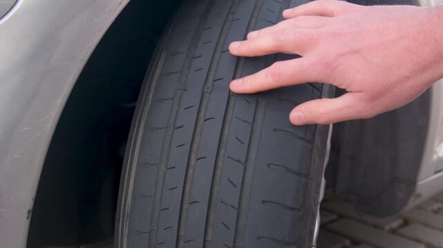 Close-up of a man's hand checking the tread wear and condition of an old car tire