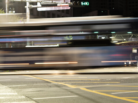 Long-exposure motion blur of a city bus passing through an urban intersection at night with light trails and road markings.