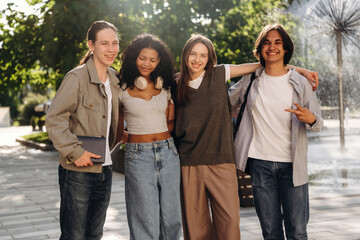 Fototapeta premium Group of four young adults smiling and posing together outdoors near a fountain in a park, wearing casual clothing with greenery in the background