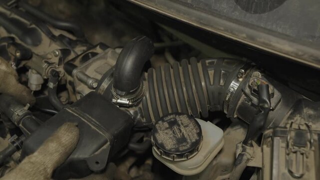Mechanic hands in gloves repairing a car engine near air intake hose.