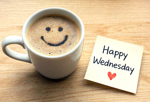 Cheerful cappuccino with a smiley face on foam beside happy wednesday note on wooden table