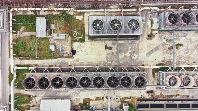 Aerial view shows large cooling towers and various equipment on the rooftops of buildings in an industrial zone. The scene captures the layout and structure of the site.
