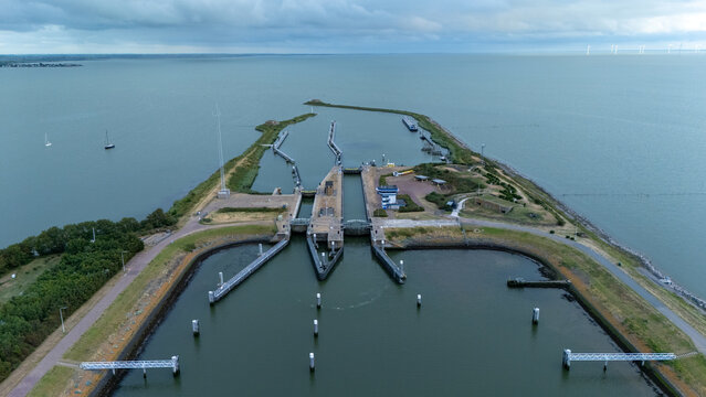 Aerial view of the Lorentz locks on the Afsluitdijk surrounded by wide open water under a cloudy sky. Dutch water management scene showing sluice gates, waterways, breakwaters and coastal infra.