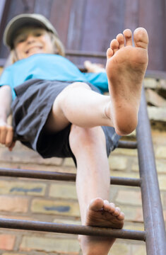 cheerful, barefoot boy on the stairs shows off his dirty bare feet. Barefoot exercises for healthy feet. An interesting, active, carefree childhood, joy. Low-angle view.