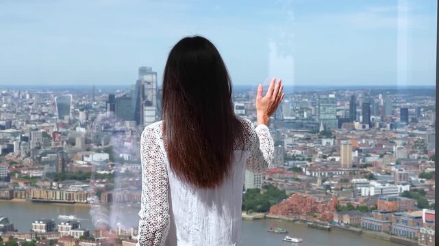 Rear view of a tourist woman looking at the panoramic view of the skyline of London, England, during a sunny summer day
